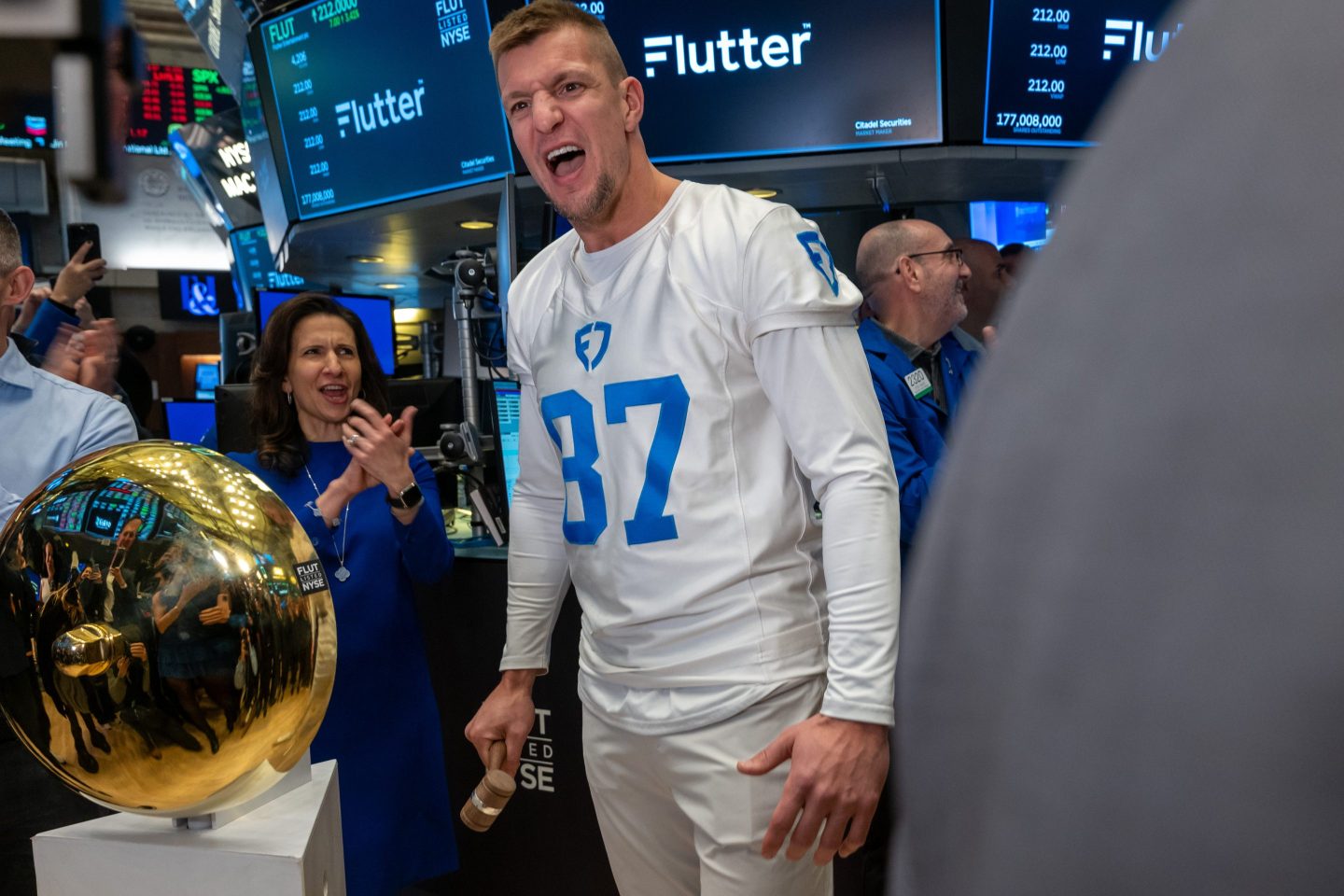 Rob Gronkowski, wearing a white and blue jersey, screams as he stands in the middle of the NYSE trading floor.