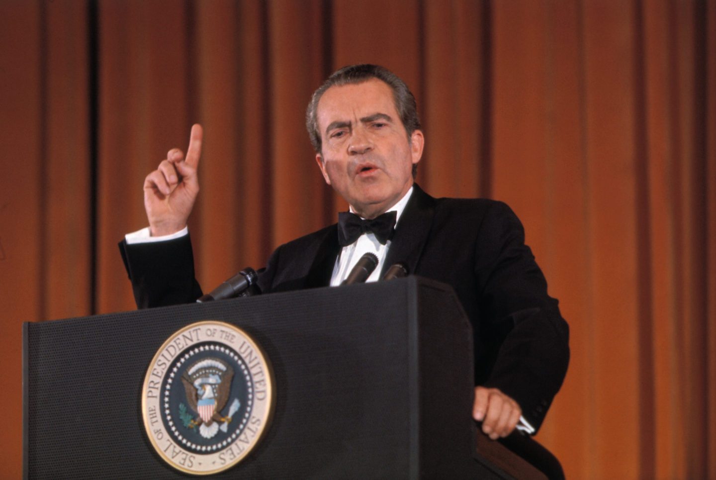 Richard Nixon stands behind a podium, one finger waving in the air as he speaks.