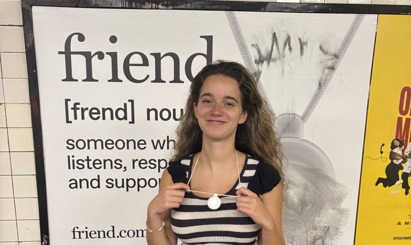 Eva Roytburg shows off her friend.com necklace in front of a poster advertising the friend